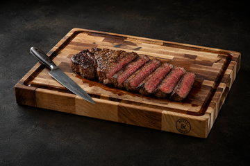 Sliced medium-rare steak on a thick end-grain maple cutting board with a juice groove catching the juices
