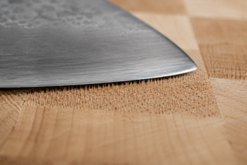 Macro close-up of a chef's knife edge resting between the upright wood fibers of an end-grain maple cutting board
