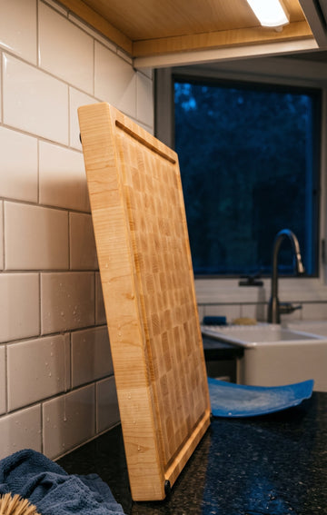 End-grain maple cutting board standing on edge to dry beside a kitchen sink