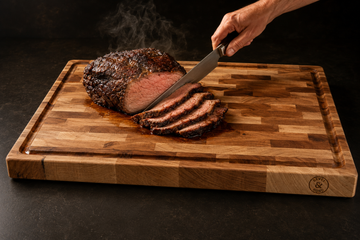 Thick end-grain maple cutting board with a juice groove catching juices from a carved roast