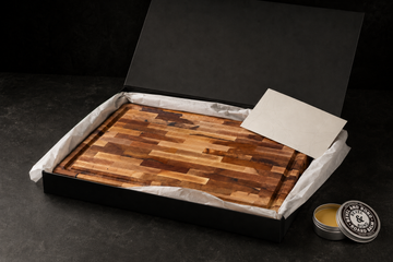 Bevel & Bond maple cutting board in its black gift box with tissue, care card, and a Board Balm tin